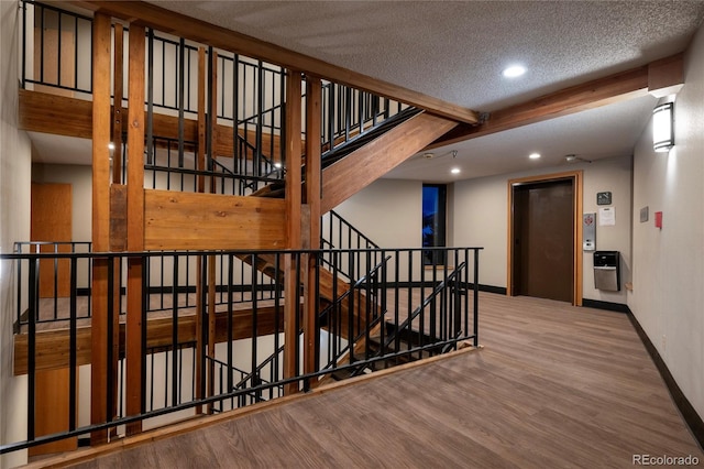 stairs with wood-type flooring, a textured ceiling, elevator, and beam ceiling