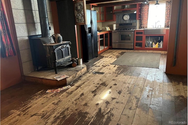 kitchen featuring light hardwood / wood-style floors, stainless steel gas stove, black fridge with ice dispenser, and a wood stove