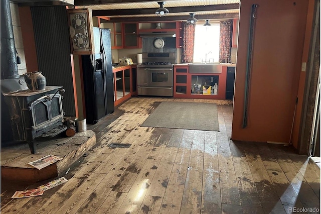 kitchen featuring beamed ceiling, sink, a wood stove, wood-type flooring, and black appliances