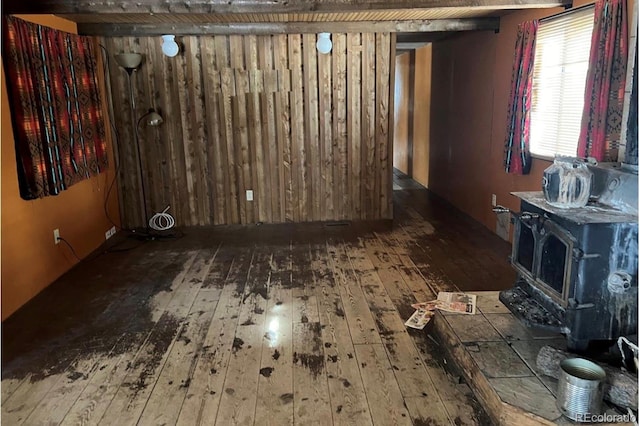 unfurnished room featuring hardwood / wood-style flooring, beam ceiling, and a wood stove