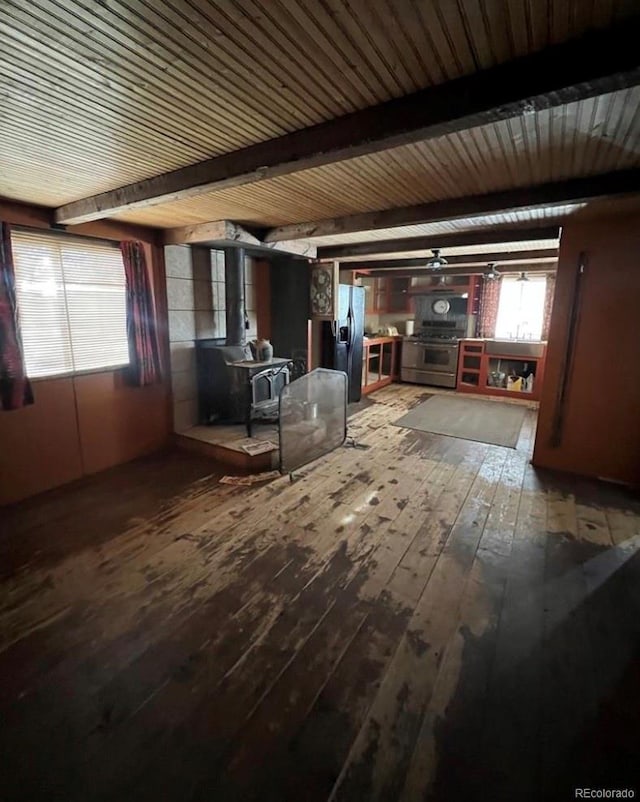 interior space with a wood stove, beam ceiling, hardwood / wood-style flooring, and a healthy amount of sunlight