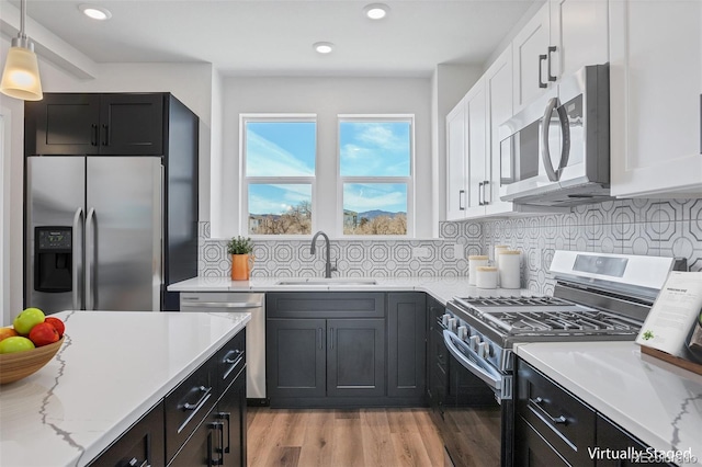 kitchen with pendant lighting, sink, white cabinets, backsplash, and stainless steel appliances