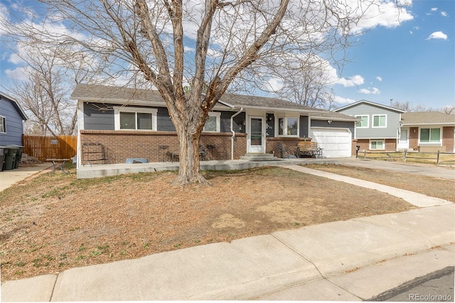 split level home with fence, an attached garage, brick siding, and concrete driveway