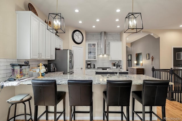 kitchen featuring white cabinetry, wall chimney range hood, stainless steel fridge, and a kitchen bar