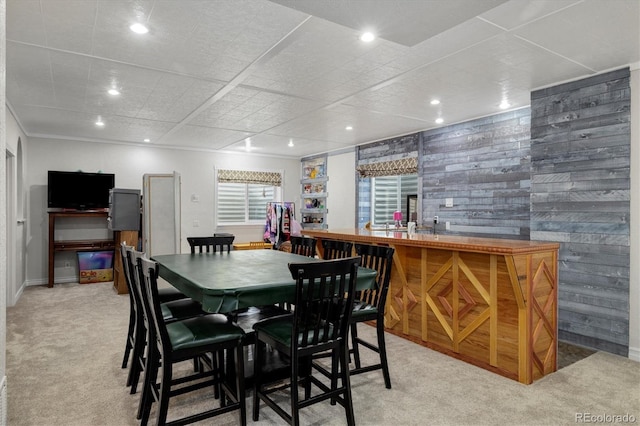 dining area with indoor bar, light carpet, and wood walls