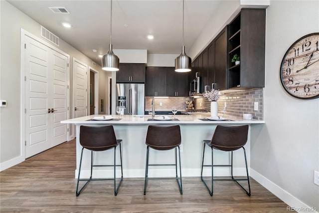 kitchen with pendant lighting, wood-type flooring, kitchen peninsula, appliances with stainless steel finishes, and dark brown cabinetry