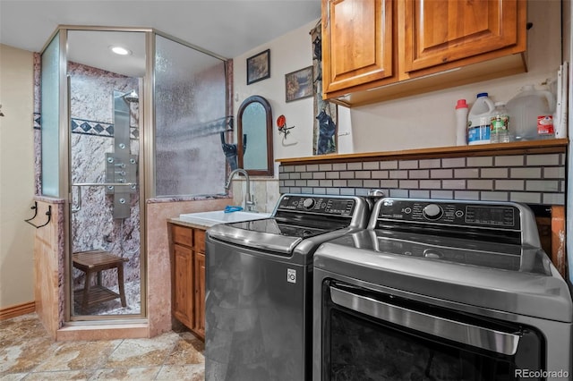 laundry room featuring cabinet space, washing machine and dryer, stone finish flooring, and a sink