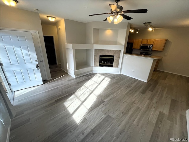 unfurnished living room with baseboards, wood finished floors, a tile fireplace, and ceiling fan