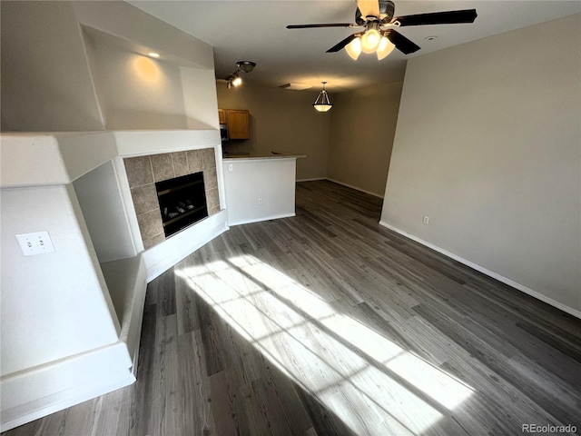 unfurnished living room featuring a tile fireplace, baseboards, dark wood-type flooring, and ceiling fan