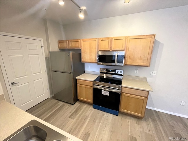 kitchen featuring baseboards, light brown cabinetry, light countertops, light wood-style floors, and stainless steel appliances