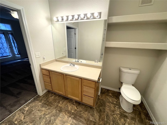 half bathroom with vanity, toilet, baseboards, and visible vents