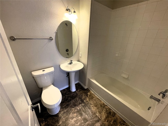 bathroom featuring toilet, a sink, baseboards, bathing tub / shower combination, and a textured wall