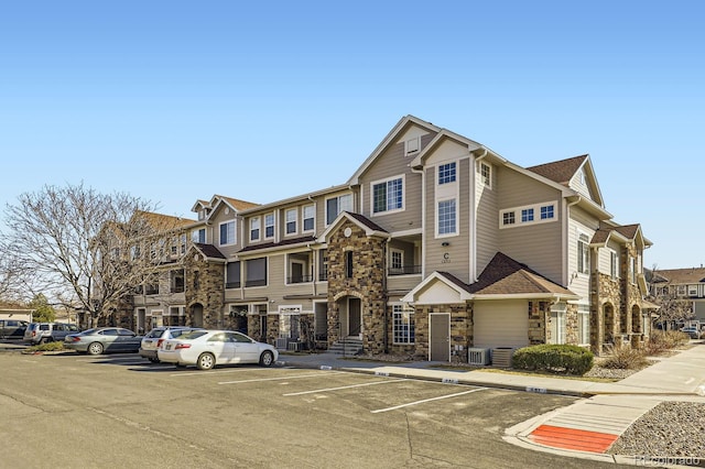 view of front of home with stone siding, a residential view, central AC, and uncovered parking