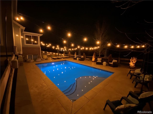 pool at night featuring a patio area