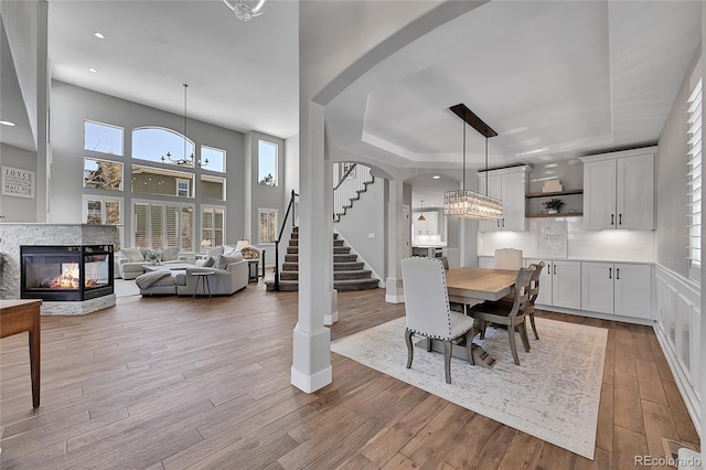 dining room featuring an inviting chandelier, a multi sided fireplace, a raised ceiling, and light wood-type flooring