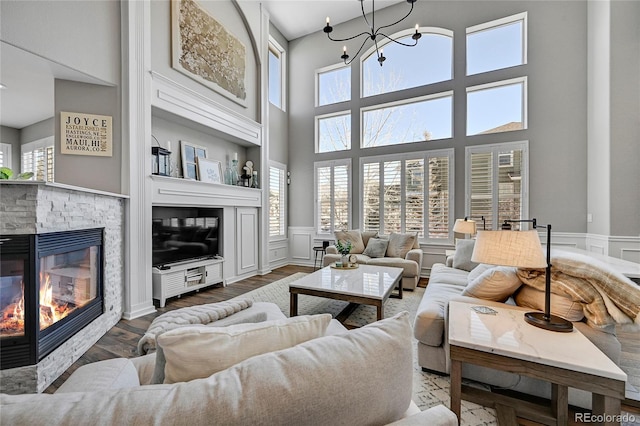 living room with a wainscoted wall, an inviting chandelier, a fireplace, and a high ceiling