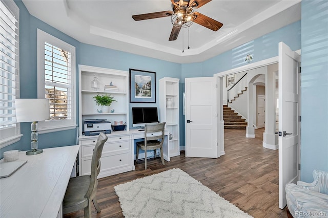 home office with a tray ceiling, ceiling fan, built in study area, and dark wood-type flooring
