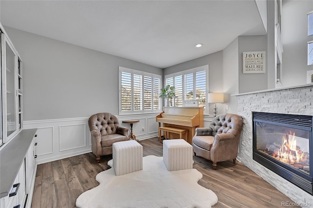 living area featuring recessed lighting, a stone fireplace, a decorative wall, a wainscoted wall, and wood finished floors