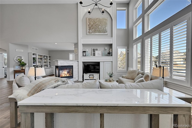 living room with a glass covered fireplace, visible vents, a high ceiling, and wood finished floors