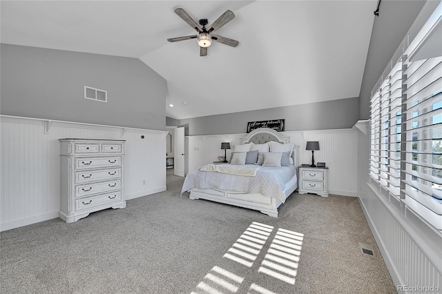 carpeted bedroom featuring wainscoting, lofted ceiling, a ceiling fan, and visible vents