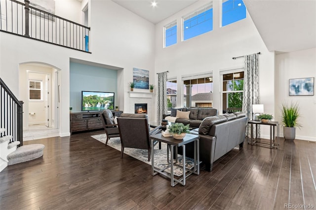 19894 W 94th Ln, Arvada, CO 80007 - living area featuring a glass covered fireplace, stairs, a high ceiling, dark wood-style flooring, and arched walkways