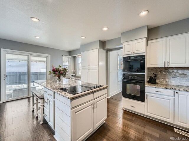 kitchen with white cabinets, dark hardwood / wood-style floors, a center island, and light stone countertops