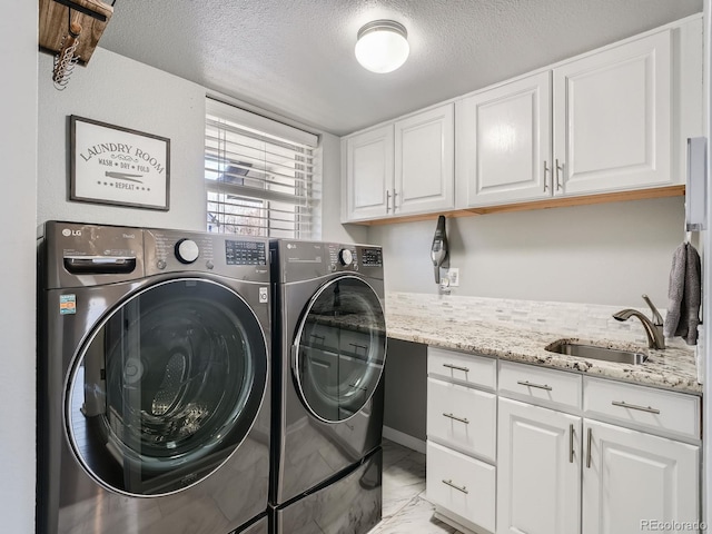 clothes washing area with cabinets, washing machine and dryer, sink, and a textured ceiling