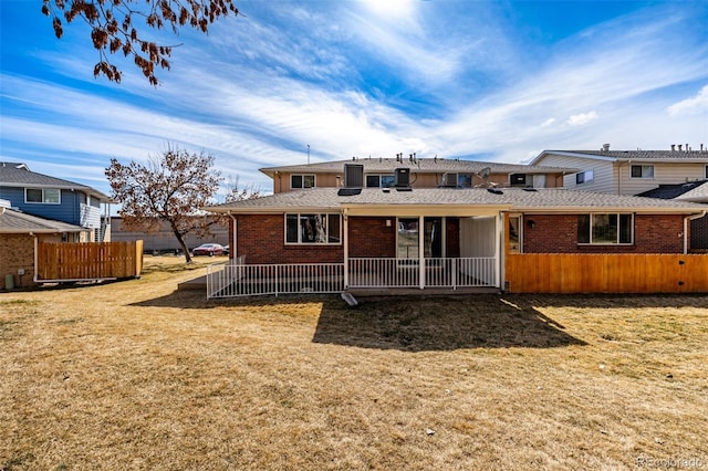 rear view of house with brick siding, roof with shingles, a yard, and fence