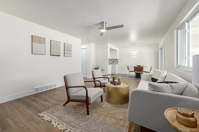 living room with ceiling fan, visible vents, baseboards, and wood finished floors