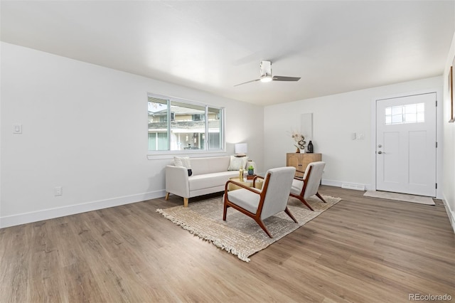 living room featuring visible vents, baseboards, a ceiling fan, and light wood finished floors