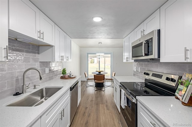 kitchen featuring light wood finished floors, decorative backsplash, appliances with stainless steel finishes, white cabinetry, and a sink