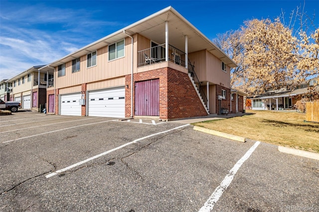 view of property featuring a balcony, a residential view, an attached garage, a front yard, and brick siding