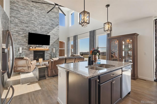 kitchen featuring a kitchen island with sink, sink, light stone countertops, a fireplace, and stainless steel appliances