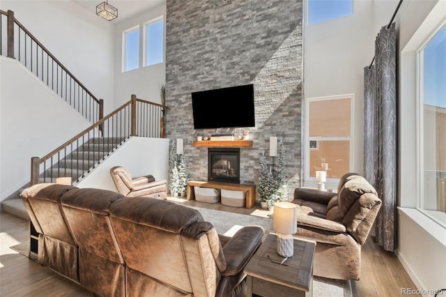 living room with a towering ceiling, light wood-type flooring, and a stone fireplace