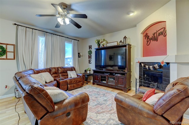 living room with a tiled fireplace, light hardwood / wood-style flooring, and ceiling fan