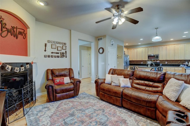 living room featuring a tile fireplace, ceiling fan, and light wood-type flooring