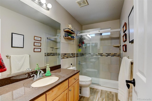 bathroom featuring a shower with door, vanity, wood-type flooring, and toilet