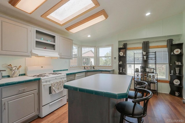 kitchen featuring white appliances, sink, vaulted ceiling with skylight, light hardwood / wood-style floors, and a kitchen island