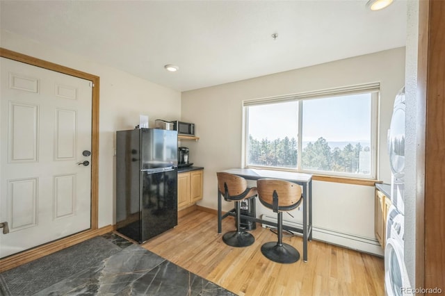 kitchen featuring black refrigerator, stacked washer and dryer, and light hardwood / wood-style flooring