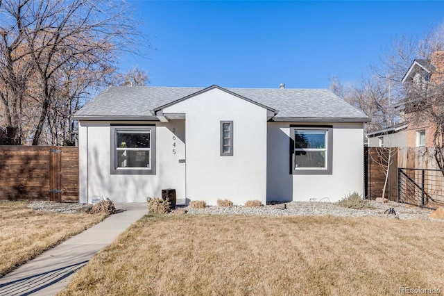 bungalow-style home featuring a shingled roof, a front yard, fence, and stucco siding