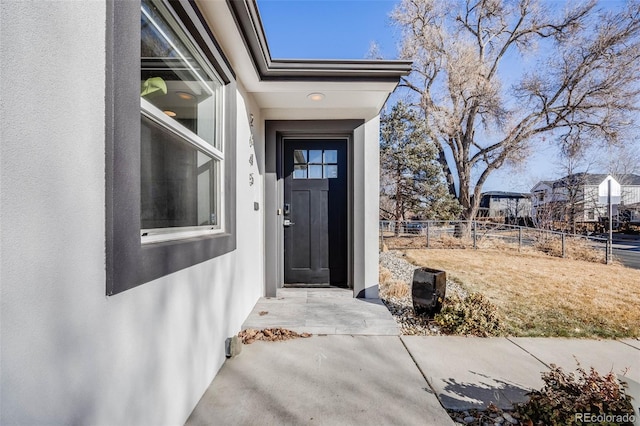 view of exterior entry with fence and stucco siding