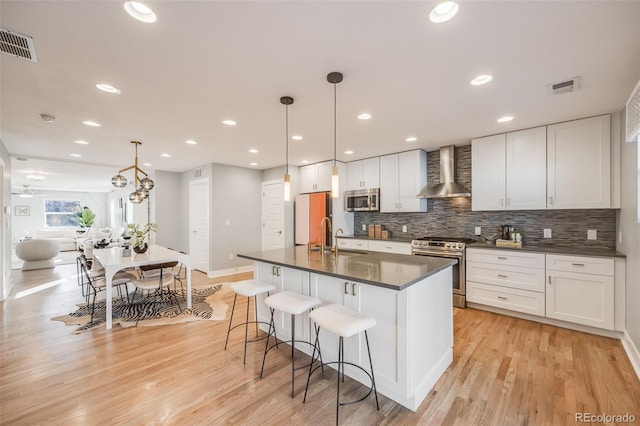 kitchen with appliances with stainless steel finishes, dark countertops, visible vents, and wall chimney range hood