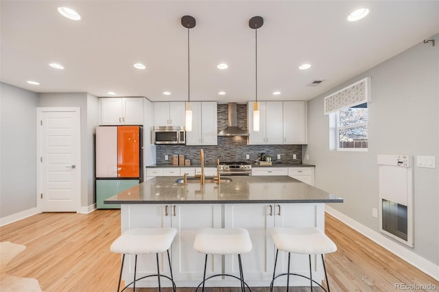 kitchen featuring appliances with stainless steel finishes, a sink, wall chimney range hood, and a kitchen bar