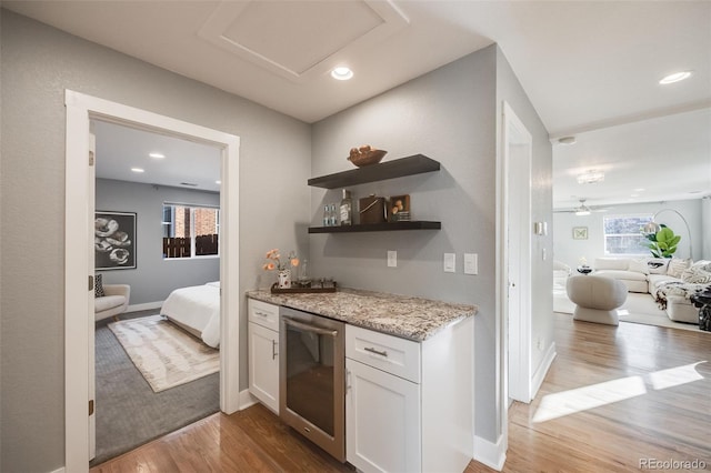 kitchen with white cabinets, wine cooler, light stone counters, open floor plan, and wood finished floors