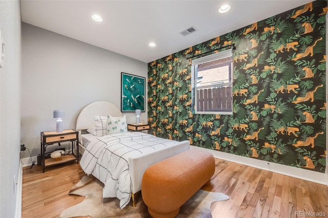 bedroom featuring wood finished floors, visible vents, baseboards, and wallpapered walls