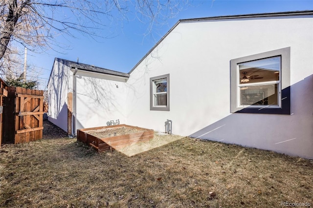 rear view of property featuring a lawn, a vegetable garden, fence, and stucco siding