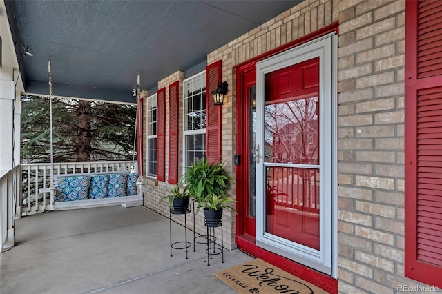 view of exterior entry with covered porch and brick siding