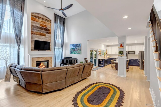 living room with light wood-style flooring, recessed lighting, a ceiling fan, a high ceiling, and a large fireplace