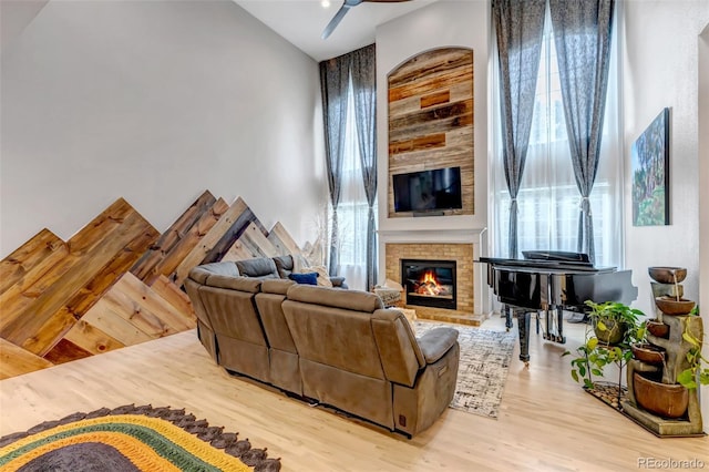 living area featuring wood finished floors, a towering ceiling, a fireplace, and a ceiling fan