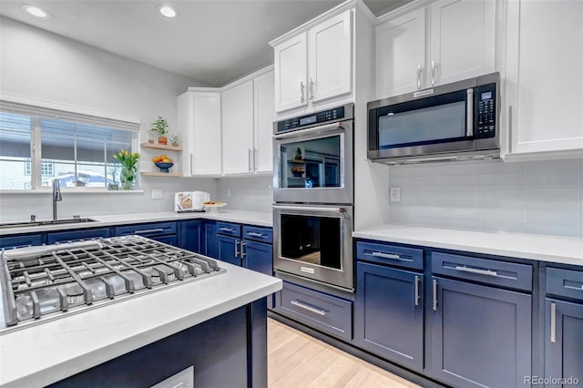 kitchen featuring white cabinets, a sink, blue cabinetry, and appliances with stainless steel finishes